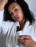 Woman holding a bottle of Zamata hair oil product against a neutral background